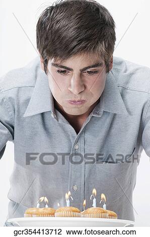 Stock Image - Man blowing out candles on cupcakes. Fotosearch