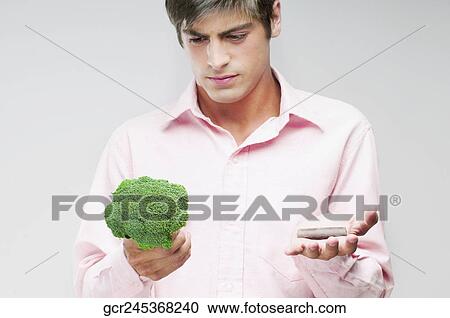 Stock Image - Man choosing between broccoli and chocolate. Fotosearch