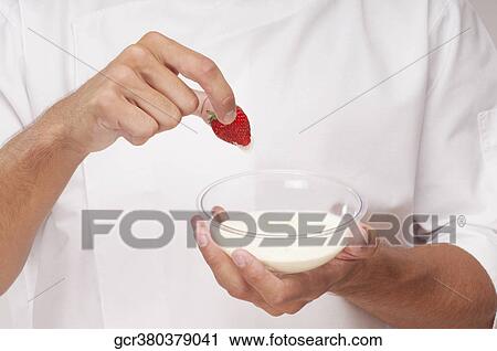 Stock Image - Man dipping a strawberry in cream. Fotosearch