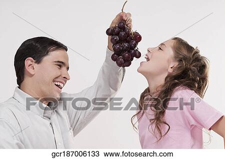 Stock Image - Man eating grapes to her daughter. Fotosearch