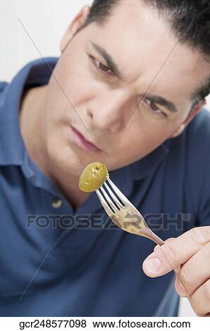 Stock Photo - Man looking at an olive on a fork. Fotosearch