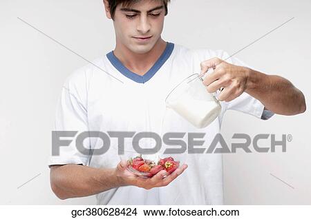 Picture - Man pouring milk on strawberries. Fotosearch