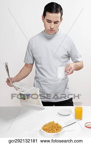 Stock Image - Man reading a newspaper at breakfast. Fotosearch