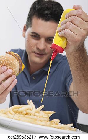 Man squeezing mustard on fries View Large Photo Image Stock Photo - Man squeezing mustard on fries. Fotosearch