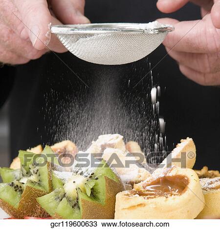 Stock Image - Mid section view of a chef sieving sugar over fruit salad. Fotosearch