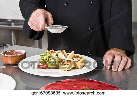 Stock Photography - Mid section view of a chef sieving sugar over fruit salad. Fotosearch