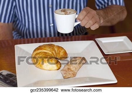 Mid section view of a man drinking coffee with a croissant and cracker in front of him View Large Photo Image Stock Image - Mid section view of a man drinking coffee with a croissant and cracker in front of him. Fotosearch