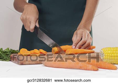 Stock Image - Mid section view of a woman cutting vegetables. Fotosearch