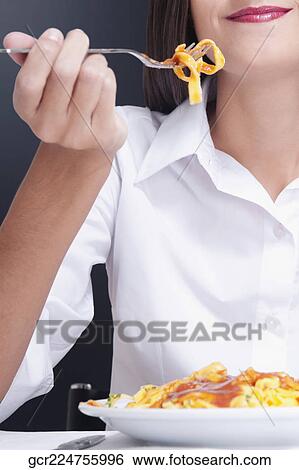 Stock Photograph - Mid section view of a woman eating pasta. Fotosearch