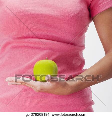 Picture - Mid section view of a woman holding a green apple. Fotosearch