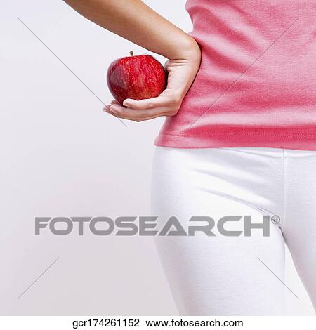 Stock Image - Mid section view of a woman holding an apple . Fotosearch