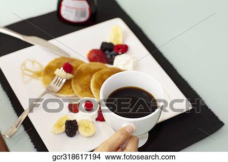 Person holding a cup of coffee over pancakes View Large Photo Image Picture - Person holding a cup of coffee over pancakes. Fotosearch