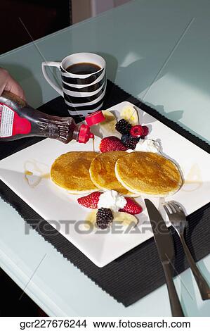Person's hand pouring syrup on pancakes View Large Photo Image Picture - Person's hand pouring syrup on pancakes. Fotosearch