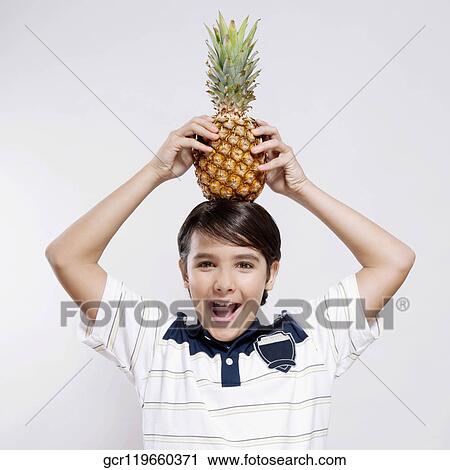 Stock Image - Portrait of a boy carrying a pineapple on his head. Fotosearch