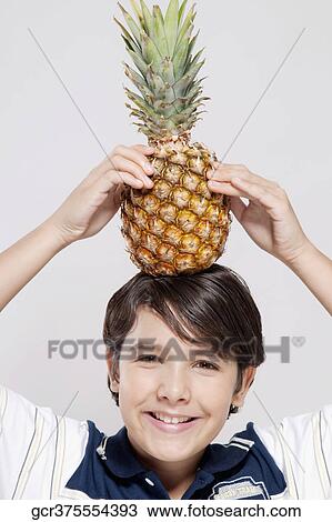 Stock Image - Portrait of a boy carrying a pineapple on his head. Fotosearch