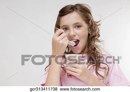 Stock Photo - Portrait of a girl eating yogurt from a cup. Fotosearch