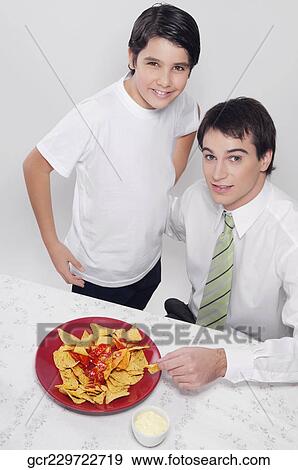Portrait of a man and his son eating nachos with salsa View Large Photo Image Stock Photo - Portrait of a man and his son eating nachos with salsa. Fotosearch