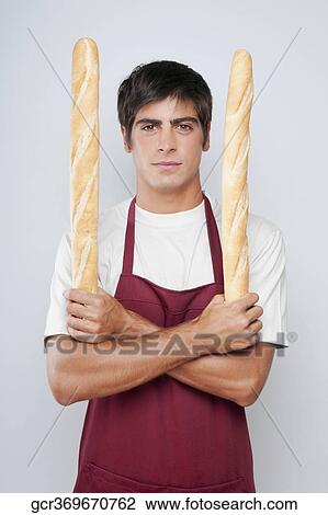 Stock Image - Portrait of a man holding baguettes in both hands. Fotosearch
