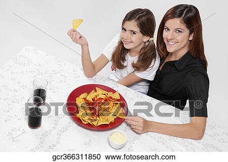 Portrait of a woman and her daughter eating nachos with salsa View Large Photo Image Stock Image - Portrait of a woman and her daughter eating nachos with salsa. Fotosearch