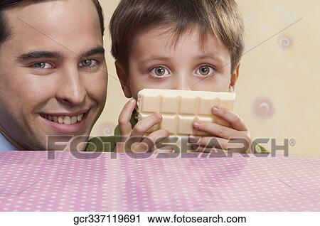 Stock Image - Portrait of man with his son holding a bar of white chocolate. Fotosearch