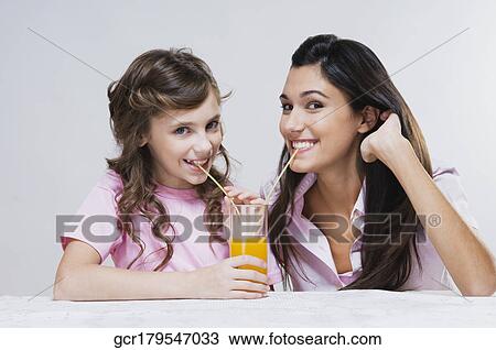 Stock Image - Portrait of mother and daughter sharing orange juice. Fotosearch