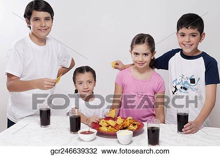 Stock Image - Portrait of two boys and two girls eating nachos from a platter. Fotosearch