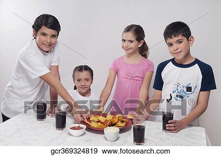 Stock Photo - Portrait of two boys and two girls eating nachos from a platter. Fotosearch