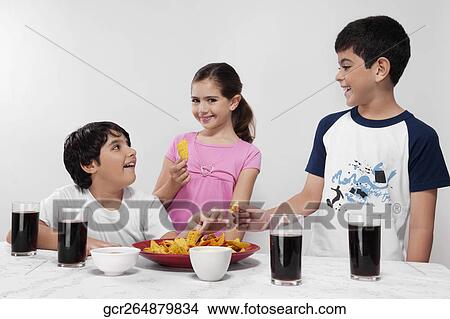 Picture - Two boys and a girl eating nachos with cola beverages. Fotosearch