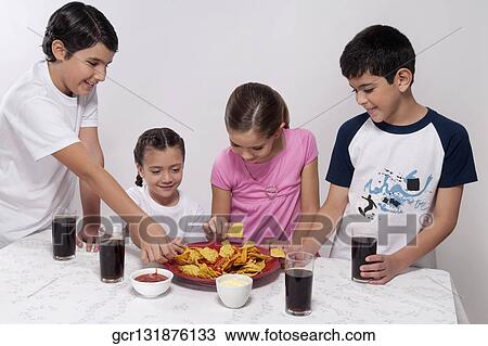 Two boys and two girls eating nachos from a platter View Large Photo Image Stock Image - Two boys and two girls eating nachos from a platter. Fotosearch