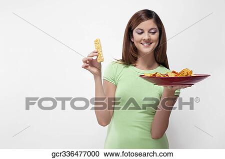 Woman choosing between a protein bar and a platter of nachos View Large Photo Image Stock Image - Woman choosing between a protein bar and a platter of nachos. Fotosearch