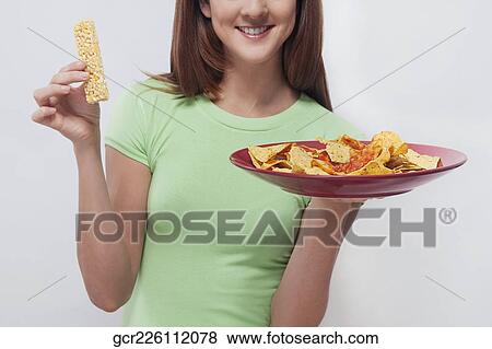 Woman choosing between a protein bar and a platter of nachos View Large Photo Image Stock Photo - Woman choosing between a protein bar and a platter of nachos. Fotosearch