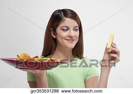 Woman choosing between a protein bar and a platter of nachos View Large Photo Image Stock Photo - Woman choosing between a protein bar and a platter of nachos. Fotosearch