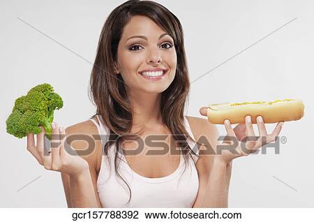 Stock Image - Woman choosing between broccoli and a hot dog. Fotosearch