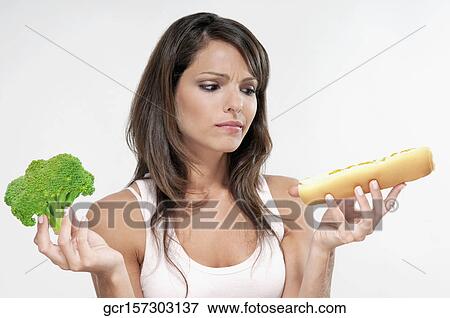 Woman choosing between broccoli and a hot dog View Large Photo Image Stock Photo - Woman choosing between broccoli and a hot dog. Fotosearch