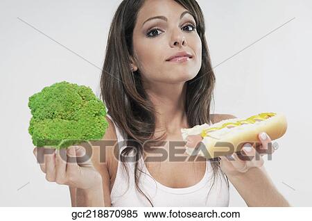Woman choosing between broccoli and a hot dog View Large Photo Image Stock Photography - Woman choosing between broccoli and a hot dog. Fotosearch