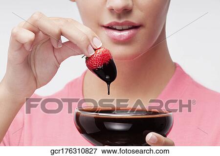 Stock Photo - Woman dipping a strawberry in chocolate sauce. Fotosearch