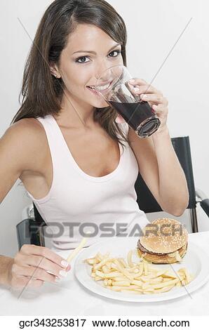 Stock Photo - Woman drinking a cola with hamburger and fries. Fotosearch