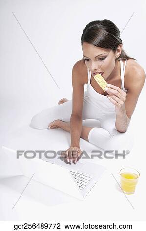 Woman eating a snack and working on a laptop View Large Photo Image Stock Image - Woman eating a snack and working on a laptop. Fotosearch