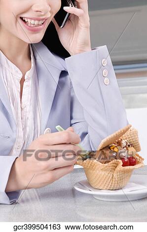 Stock Image - Woman eating ice cream and talking on a mobile phone. Fotosearch