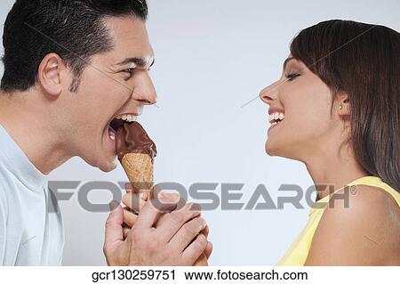Stock Image - Woman feeding an ice cream cone to her husband. Fotosearch