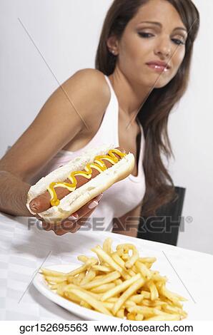 Stock Image - Woman frowning at a hot dog. Fotosearch