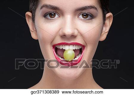 Stock Photo - Woman holding a grape between her teeth. Fotosearch