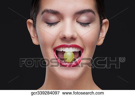Stock Photo - Woman holding a green grape between her teeth. Fotosearch
