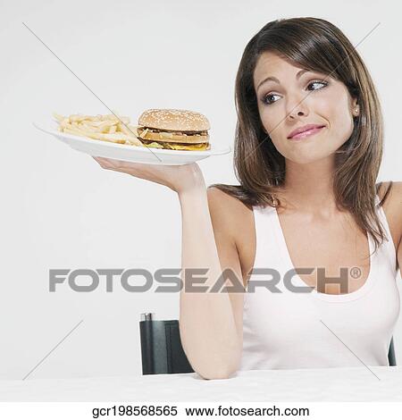 Woman holding a hamburger in one hand and frowning View Large Photo Image Stock Photography - Woman holding a hamburger in one hand and frowning. Fotosearch