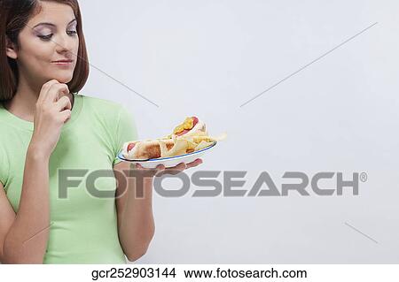 Picture - Woman holding a plate of hot dog and thinking. Fotosearch