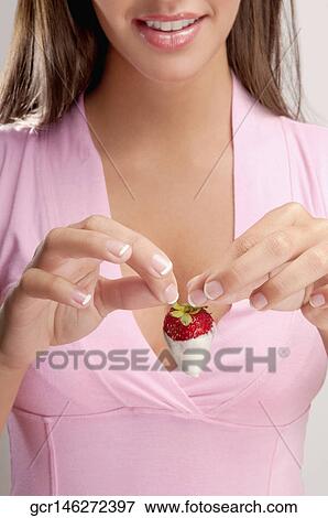 Stock Photo - Woman holding a strawberry dipped in cream and smiling. Fotosearch
