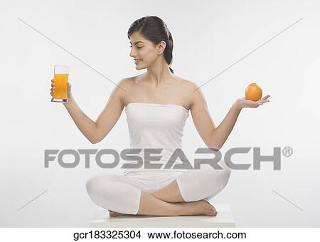 Picture - Woman holding an orange and a glass of orange juice. Fotosearch
