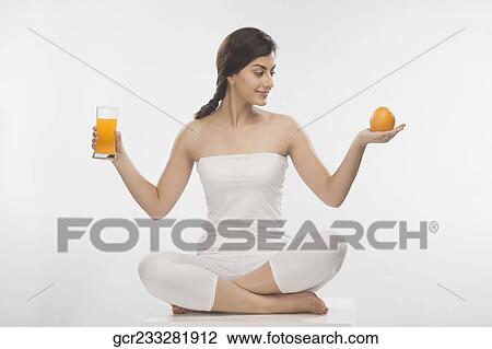 Stock Image - Woman holding an orange and a glass of orange juice. Fotosearch