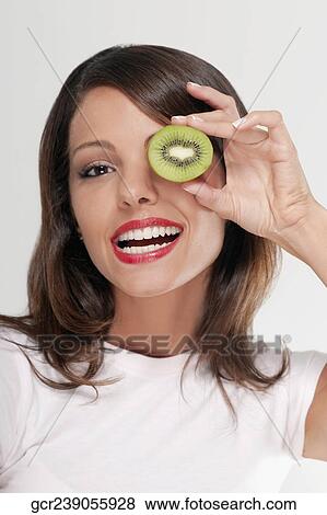 Stock Photo - Woman holding half a kiwi over her eye. Fotosearch