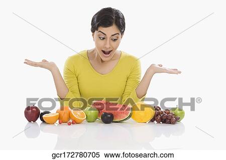 Stock Photography - Woman looking at assorted fresh fruits and gesturing. Fotosearch